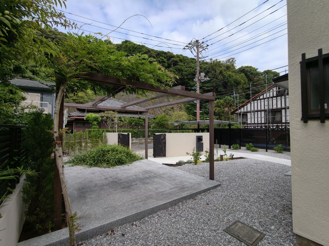 藤を絡ませた木製パーゴラ。梁の先には鋳物門扉「ロヴァンティ」とポストが見える
